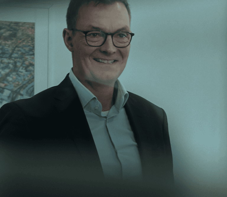 Zwei Mitarbeiter von GEDIA stehen im Anzug in einem Raum und freuen sich. 